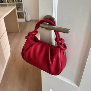 Detailed view of a red pleated dumpling bag hanging on a modern door handle