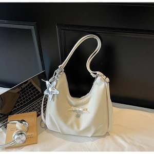 Detail of cream white dumpling bag with silver star charm and bow accessory on a desk