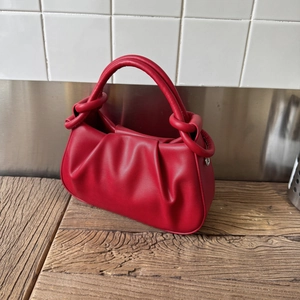 Close-up of bright red ruched shoulder bag with knot detail and half-moon structure