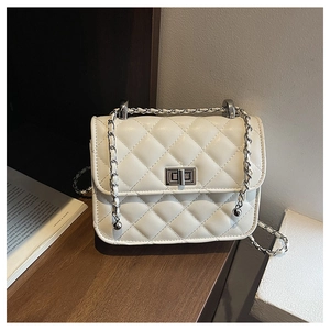 Detailed macro shot of white quilted crossbody bag with silver rotating clasp on wooden desk