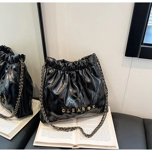 Detail view of black quilted bucket bag with gold metal letters and chain strap