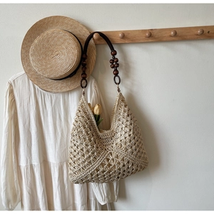 Detail of woven straw tote bag with decorative dark wood beads on shoulder strap