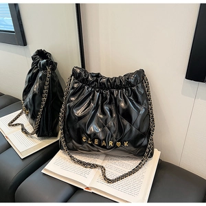 Detail of glossy quilted leather texture and gold metal logo on black bucket bag