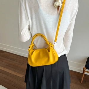 Detail of a bright yellow pleated cloud bag worn by a model in a minimalist room