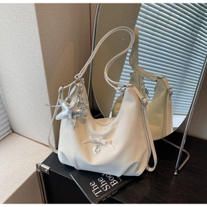 Detail view of cream-white hobo bag with bow decor, heart charm, and silver starfish pendant