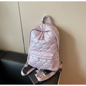 Detail view of lavender quilted backpack with front zipper pocket on a leather surface