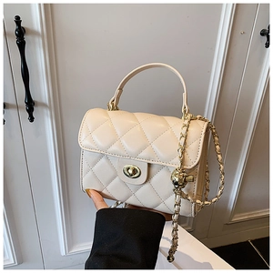 Detail of cream quilted handbag with gold turn-lock and chain strap held by hand