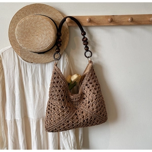 Detailed view of woven straw tote bag with brown wooden bead handle on a wall hook