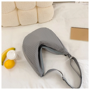 Detailansicht der grauen Karo-Halbmondtasche aus Nylon mit verstellbarem Gurt auf weißem Bett