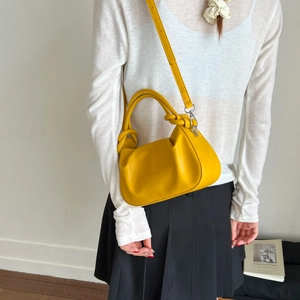 Detail of yellow pleated cloud bag featuring decorative knotted handle and slim strap