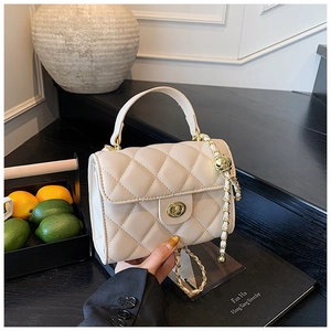 Detail of cream quilted bag showing textured finish, gold twist lock and chain strap