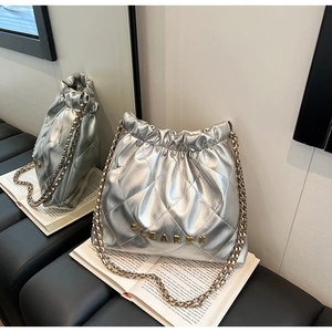 Detail of silver quilted bucket bag featuring gold chain and Clear K logo on a book