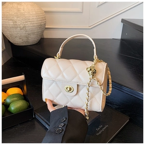 Detail of off-white quilted handbag with golden twist lock and chain strap on desk