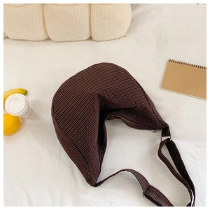 Detailansicht der dunkelbraun karierten Nylon-Halbmondtasche auf einem weißen Bett