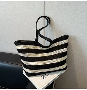 Detailed view of striped woven tote bag featuring black leather handles on decorative books