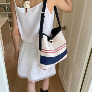 Detail of canvas tote bag featuring red and blue stripes with black leather strap