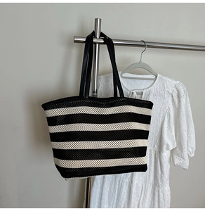 Detail of a black and white striped tote bag with leather straps on a metal hanger