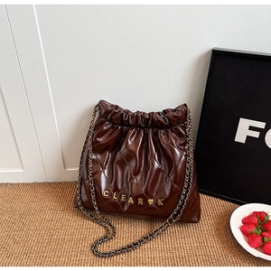 Detail of a dark brown quilted bucket bag with gold chain strap and heart logo charm