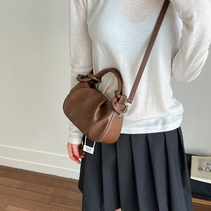 Detail of a brown pleated cloud bag with a knotted handle and detachable shoulder strap