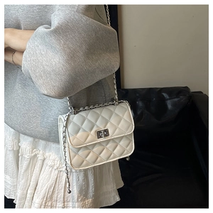 Detail of white quilted chain bag featuring silver metal clasp and leather woven strap