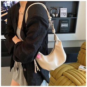 Detalle de bolso croissant crema con correa anudada y colgante de corazón rosa