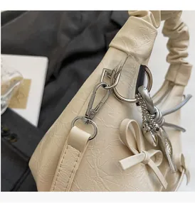 Macro detail of creamy white pleated handbag with silver hardware and bow accent