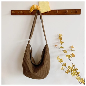 Detail einer dunkelbraun karierten Nylon-Halbmondtasche an einem schlichten Holzhaken
