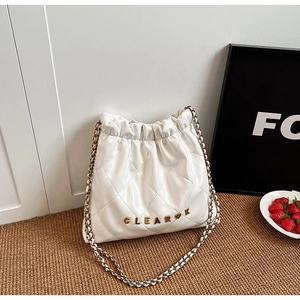 Detail of white quilted drawstring bucket bag with gold chain strap on straw mat