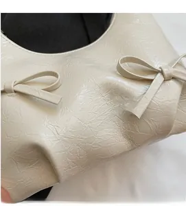 Detail of cream white pleated handbag featuring decorative bows and soft leather texture