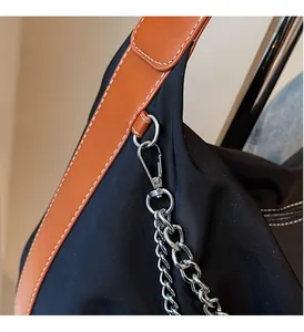 Close-up of polished silver chain hardware and brown leather strap on black nylon bag