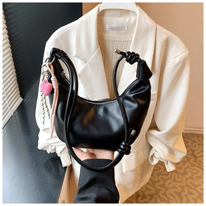 Detalle de bolso hobo negro con correa anudada y colgante de corazón rosa suave