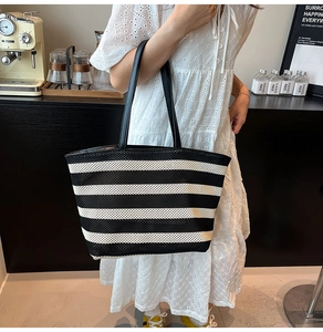 Detail of black and white striped knit tote bag held by a model in a cafe setting