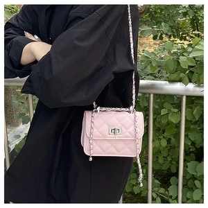 Detail of pink quilted crossbody bag with metal chain strap worn on model's shoulder