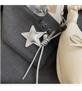 Close-up of silver star-shaped bag charm with metallic texture on off-white pleated bag