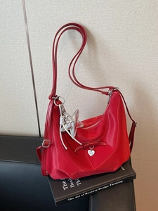 Red nylon crescent shoulder bag with heart pendant and star charm on a book