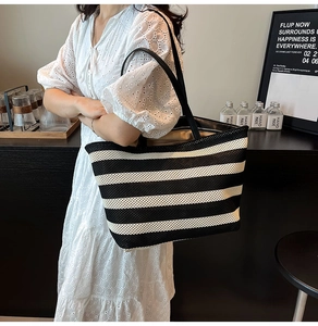 Close-up of a large woven tote bag with black and white stripes and black shoulder straps