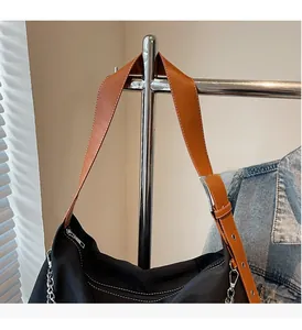 Detail of durable black nylon tote featuring a wide brown leather strap and metal chain buckle