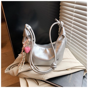 Bolso de hombro plateado metalizado con asa anudada y un colgante de corazón rosa brillante