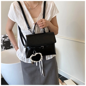 Detail of black glossy leather backpack with heart charm and metallic buckle closure