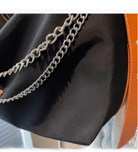 Close-up of black canvas bag with silver chain strap and orange leather shoulder strap details