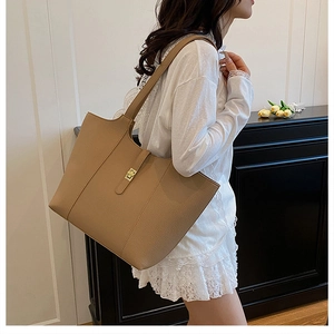 Close-up of a khaki textured tote bag with a golden metal lock worn by a model in a room