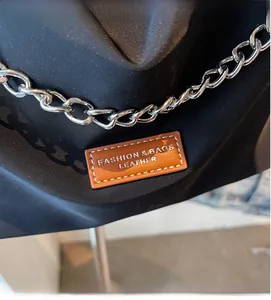 Detail view of black nylon bag featuring silver chain strap and brown leather logo patch