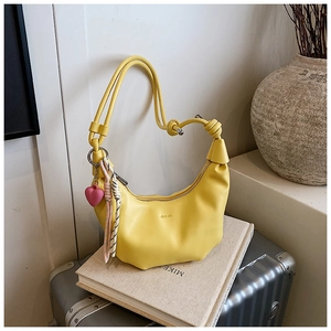 Detalle de bolso de media luna amarillo con colgante de corazón rosa en maleta