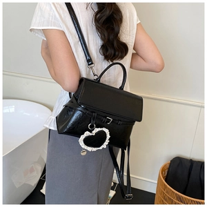 Detail of black patent leather convertible backpack with white lace heart charm accessory
