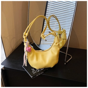 Detalle del bolso de hombro amarillo de media luna con ecocuero plisado y borla de corazón