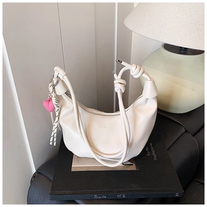 Detalle de bolso hobo crema con asa anudada y colgante de corazón rosa decorativo