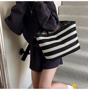 Close-up of black and white striped woven tote bag worn by a model on stairs