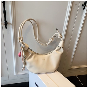 Detalle de bolso de hombro media luna crema con correa anudada y colgante rosa