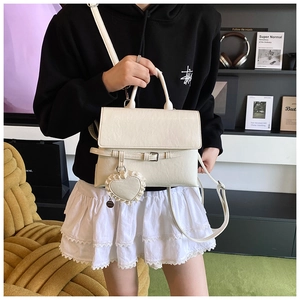 Detail of cream white structured crossbody bag with heart pendant and top handle strap