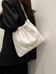 White quilted bucket bag with chain strap shown on a model in a minimalist setting